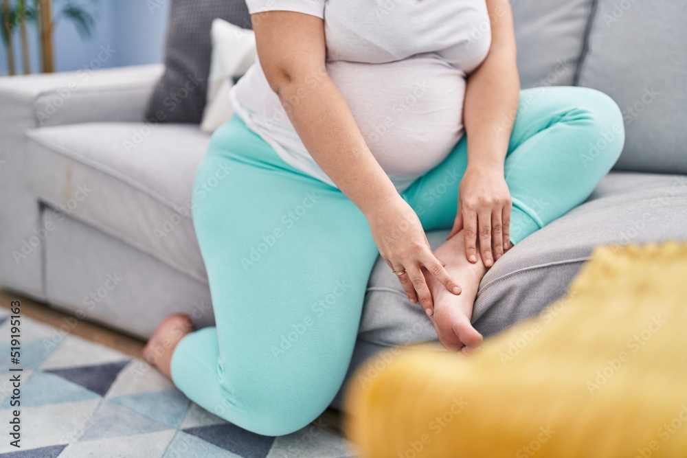 Young pregnant woman suffering for foot pain sitting on sofa at home
