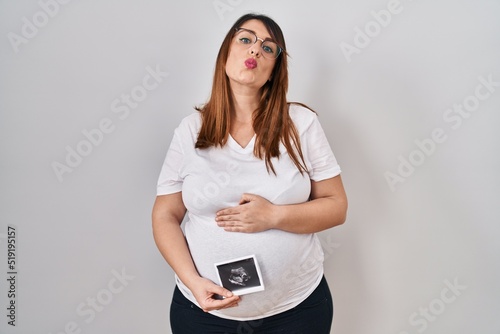 Pregnant woman holding baby ecography looking at the camera blowing a kiss being lovely and sexy. love expression.
