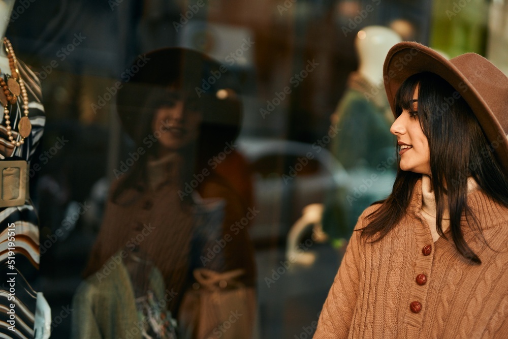 Brunette woman wearing winter hat looking at shop window outdoors at the city