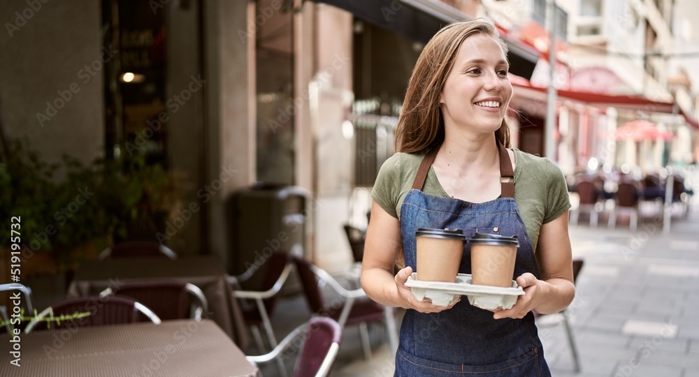 Young blonde woman wearing apron holding coffee at coffee shop Young blonde woman wearing apron holding coffee at coffee shop