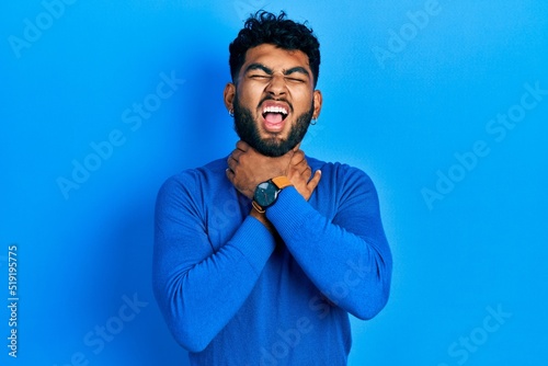 Arab man with beard wearing casual blue sweater shouting and suffocate because painful strangle. health problem. asphyxiate and suicide concept.