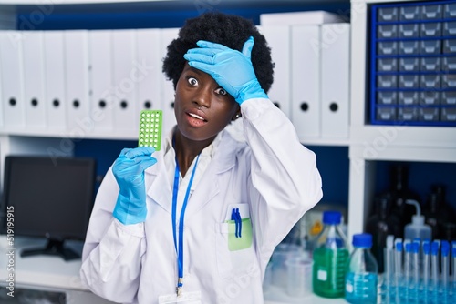 African young woman working at scientist laboratory holding birth control pills stressed and frustrated with hand on head  surprised and angry face
