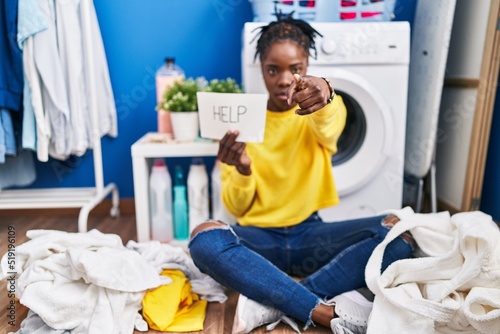 Beautiful black woman doing laundry asking for help pointing with finger to the camera and to you, confident gesture looking serious