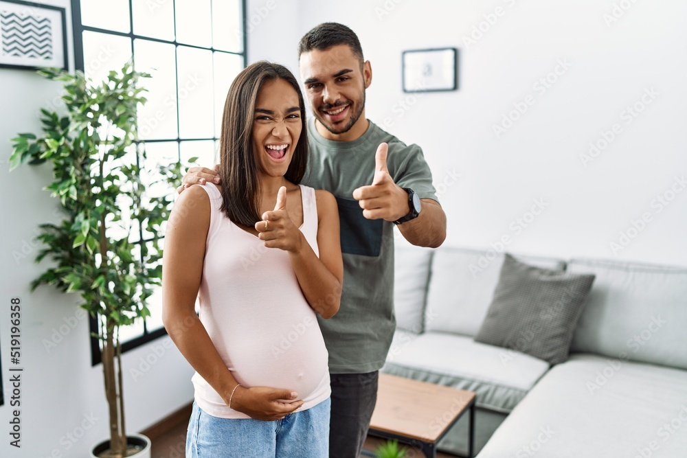 Young interracial couple expecting a baby, touching pregnant belly pointing fingers to camera with happy and funny face. good energy and vibes. Young interracial couple expecting a baby, touching pregnant belly pointing fingers to camera with happy and funny face. good energy and vibes.