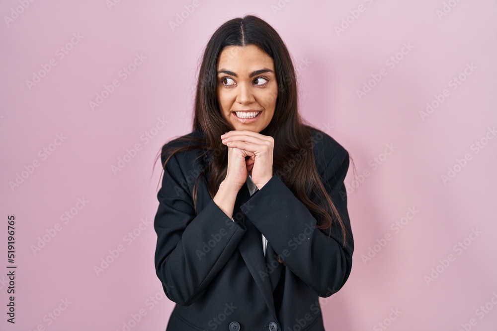 Young brunette woman wearing business style over pink background laughing nervous and excited with hands on chin looking to the side Young brunette woman wearing business style over pink background laughing nervous and excited with hands on chin looking to the side