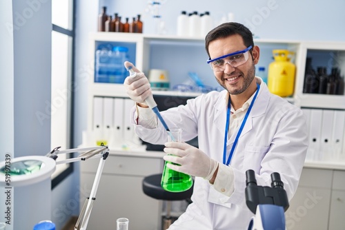 Young hispanic man scientist measuring liquid using pipette at laboratory