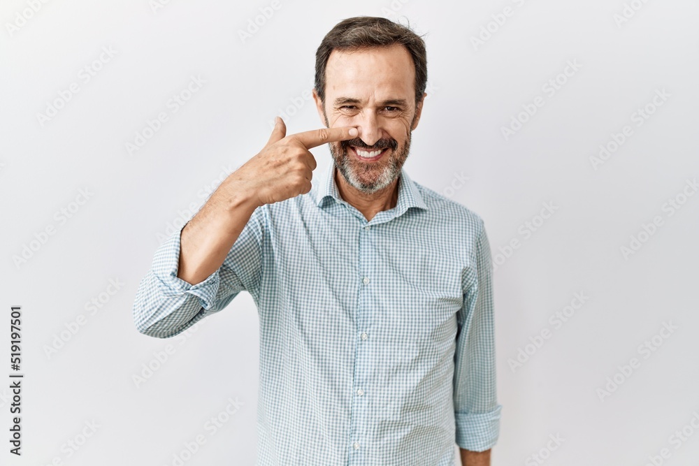 Middle age hispanic man with beard standing over isolated background pointing with hand finger to face and nose, smiling cheerful. beauty concept