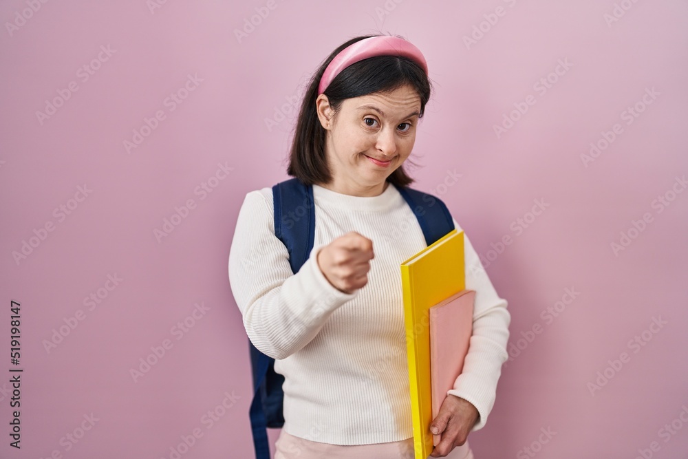 Woman with down syndrome wearing student backpack and holding books pointing fingers to camera with happy and funny face. good energy and vibes. Woman with down syndrome wearing student backpack and holding books pointing fingers to camera with happy and funny face. good energy and vibes.