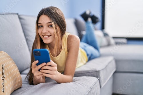 Adorable girl using smartphone lying on sofa at home