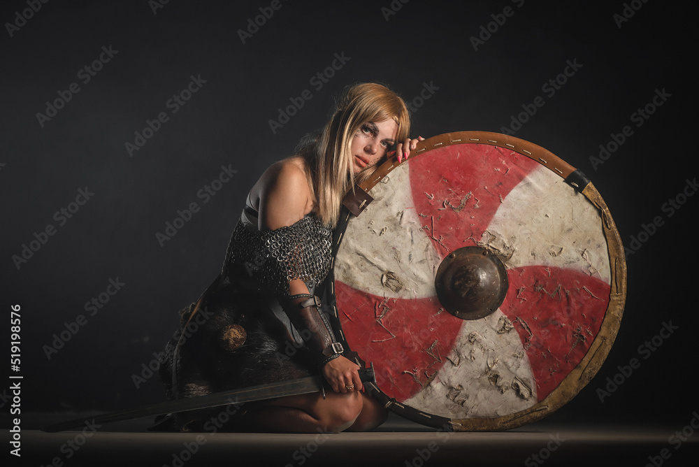 Fototapeta premium Woman warrior in the armor and with the sword and shield in hands stands on her knees. Lose the battle concept.