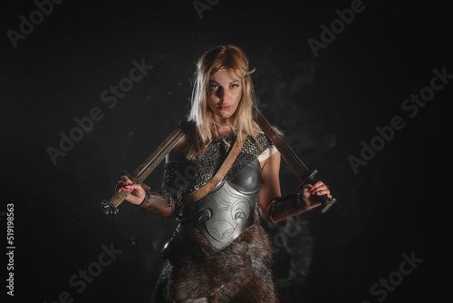 Fotografie Warrior woman in the armor stands with the two swords in the hands concept