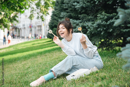 A young woman eating sushi in the park, picnic in nature.