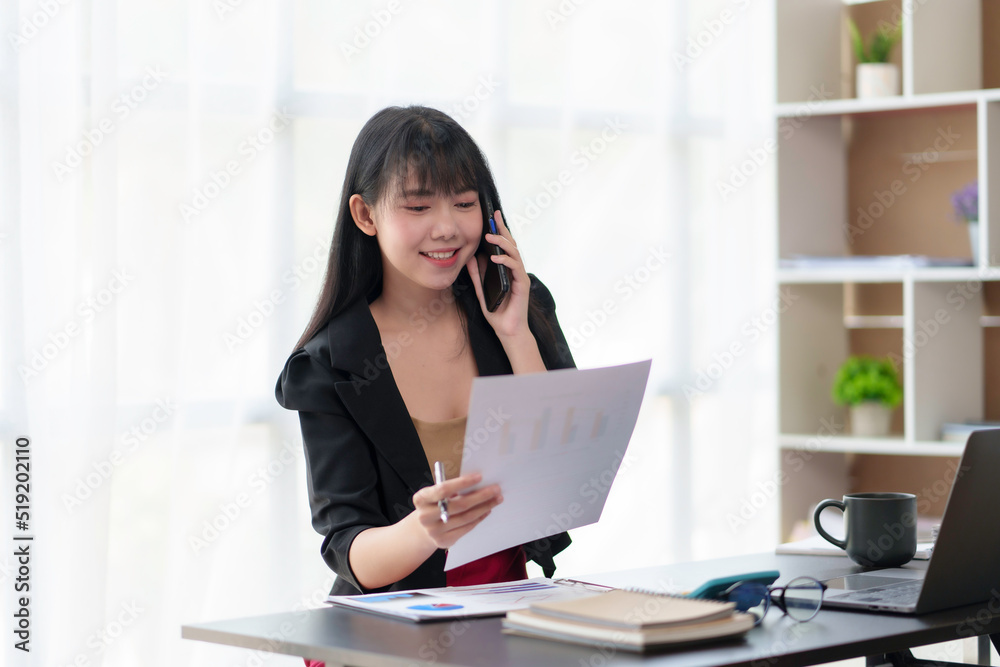 Charming and smiling Asian businesswoman chatting on mobile phone with customer in office. Charming and smiling Asian businesswoman chatting on mobile phone with customer in office.