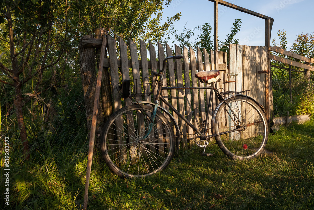 An old bicycle is parked near a wooden fence. Rural motif