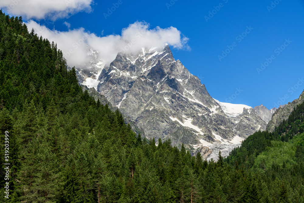 Beautiful alpian mountains landscape. High snow covered mountains green high forset on the hills under blue sky with clouds.