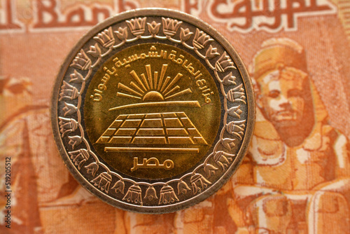 Solar farms of Aswan Egypt slogan from the obverse side of 1 LE EGP coin one Egyptian pound money on a blurred background of reverse side of one pound banknote cash money, selective focus photo