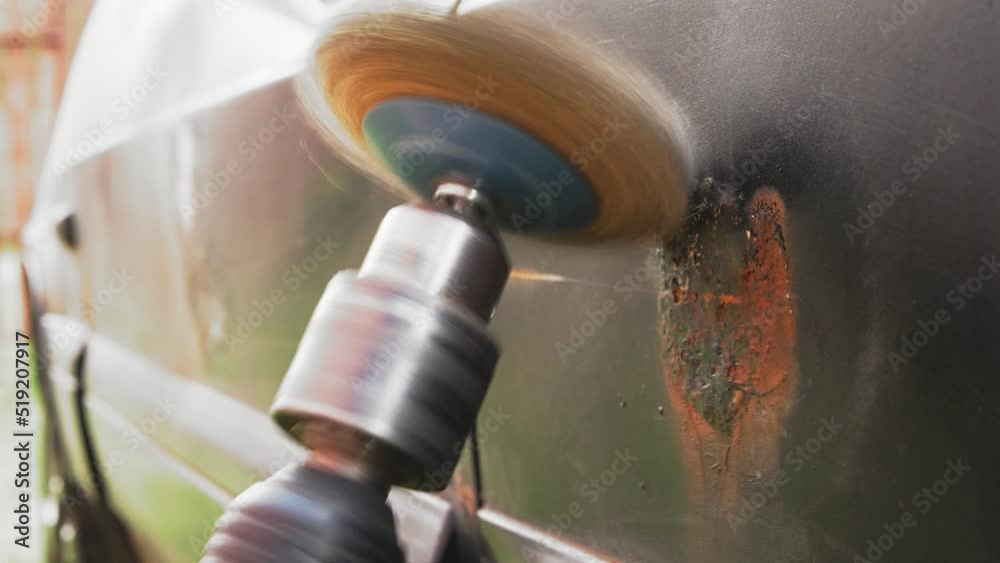 A round metal brush in the hands of the master cleans rust and paint from the car. Medium plan