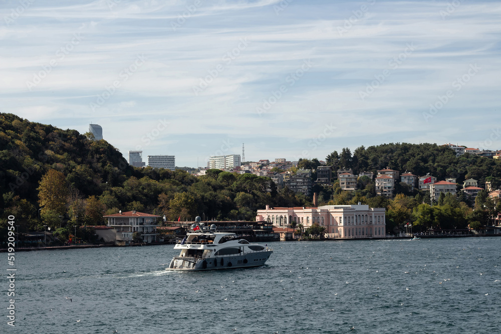 View of a yacht passing on Bosphorus and Baltalimani neighborhood on European side of Istanbul. It is a sunny summer day. Beautiful travel scene.