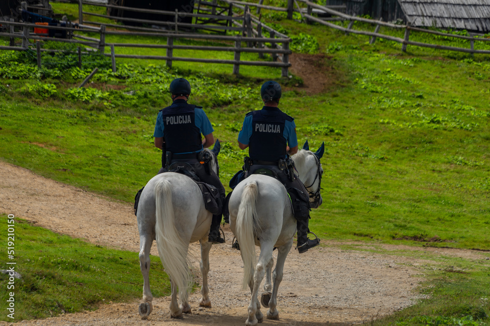 Blue policemans on white horses on path in Velika Planina mountains in holiday Blue policemans on white horses on path in Velika Planina mountains in holiday