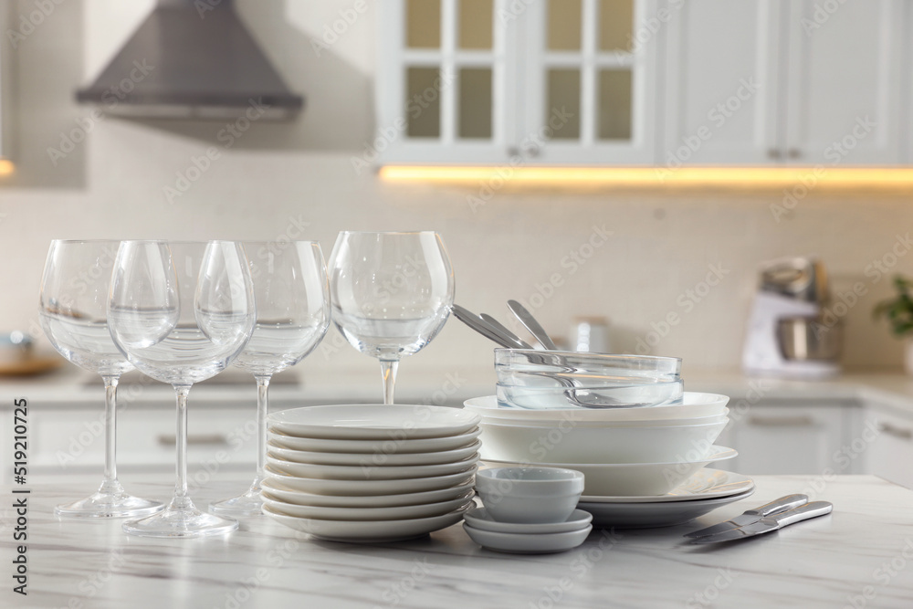 Different clean dishware, cutlery and glasses on white marble table in kitchen