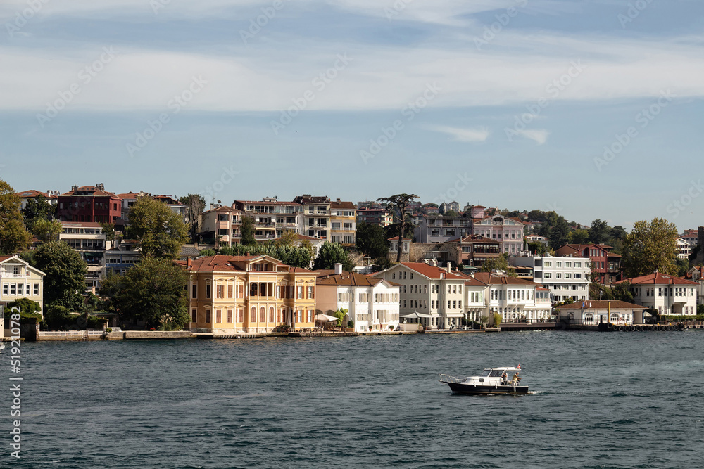 View of historical, traditional mansions by Bosphorus in Anadolu Hisari area of Asian side of Istanbul. Small fishing boat passes. It is a sunny summer day. Beautiful travel scene.