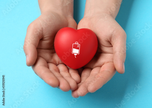Man holding red heart in hands on light blue background, top view. Blood donation concept