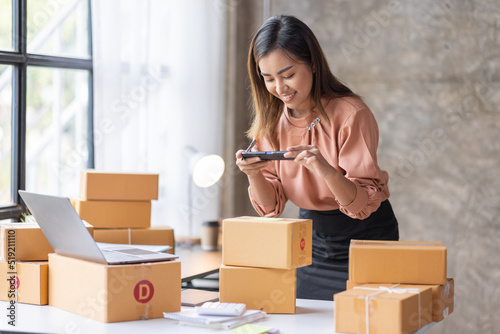 Young Asian women take photos to box addresses with cell telephone or smartphone digital camera for post to sell online on the Internet and prepare pack product boxes. Selling SME online ideas concept © David