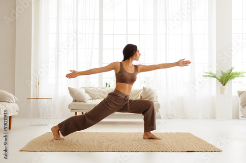 Side view of brunette woman practicing yoga pose on carpet in living room 