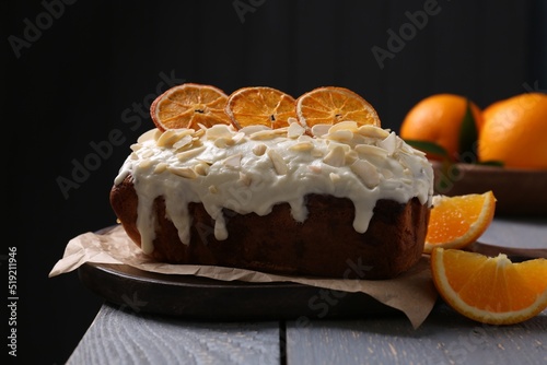 Delicious sweet cake with dry orange and almond petals on grey wooden table