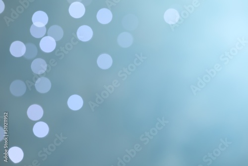 Blurred view of festive lights on light blue background, space for text. Bokeh effect