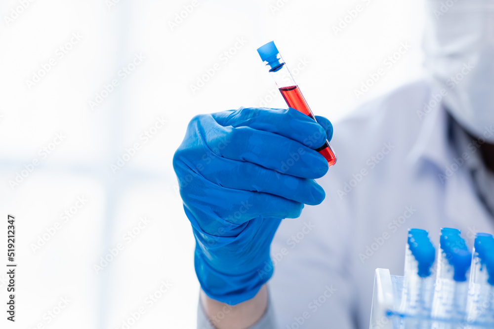 Lab assistant, a medical scientist, a chemistry researcher holds a glass tube through the blood sample, does a chemical experiment and examines a patient's blood sample. Medicine and research concept. Lab assistant, a medical scientist, a chemistry researcher holds a glass tube through the blood sample, does a chemical experiment and examines a patient's blood sample. Medicine and research concept.