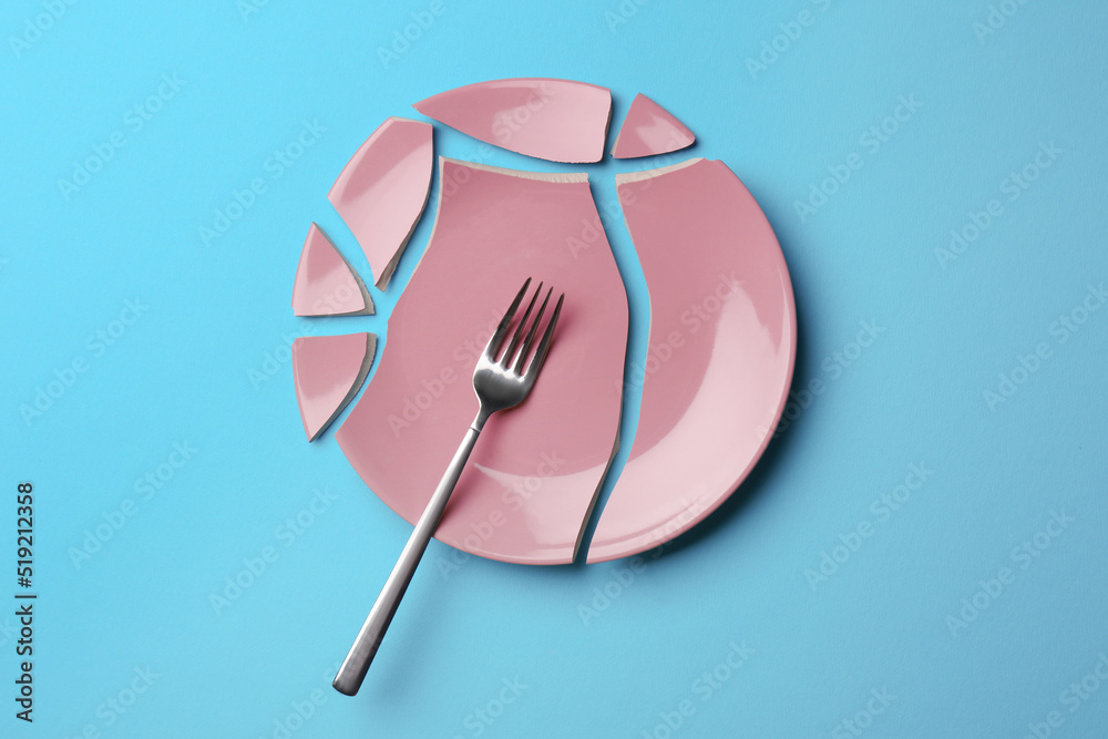 Pieces of broken ceramic plate and fork on light blue background, flat lay Pieces of broken ceramic plate and fork on light blue background, flat lay
