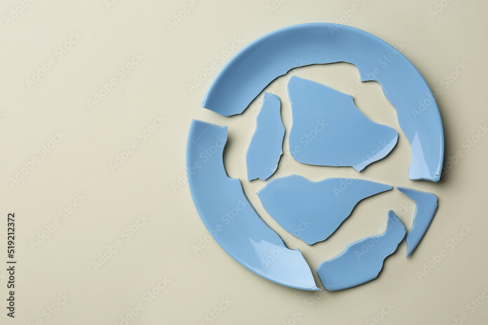 Pieces of broken ceramic plate on beige background, top view. Space for text Pieces of broken ceramic plate on beige background, top view. Space for text