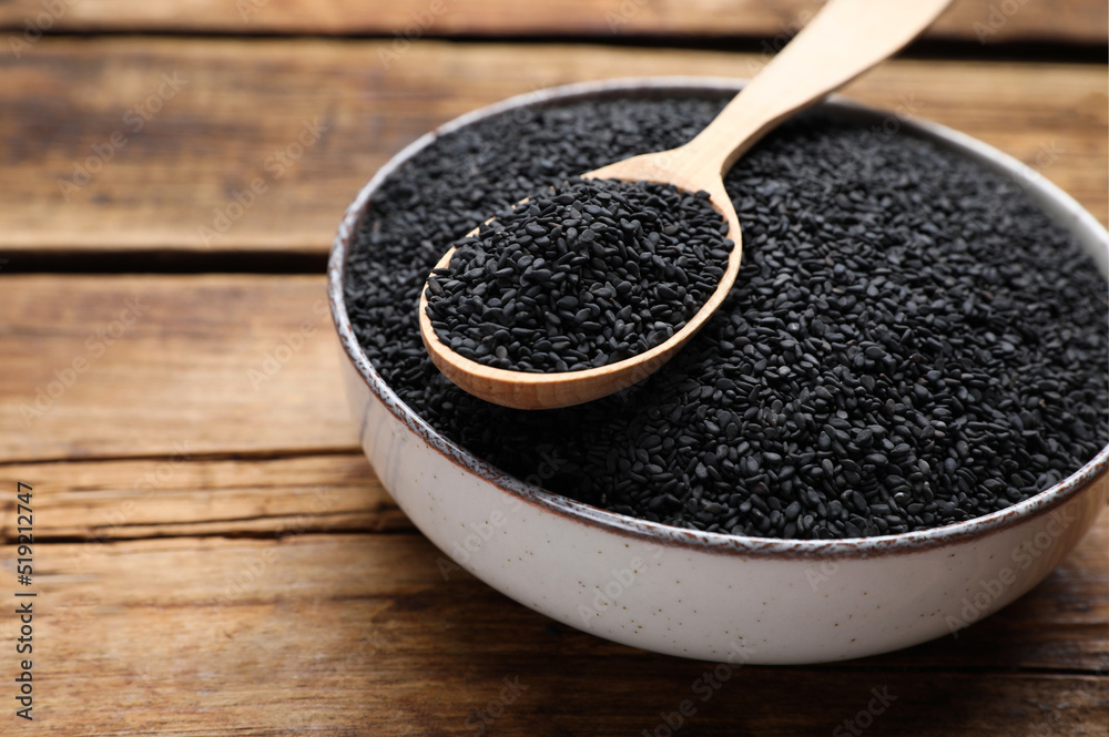 Bowl and spoon with black sesame on wooden table, closeup. Space for text Bowl and spoon with black sesame on wooden table, closeup. Space for text