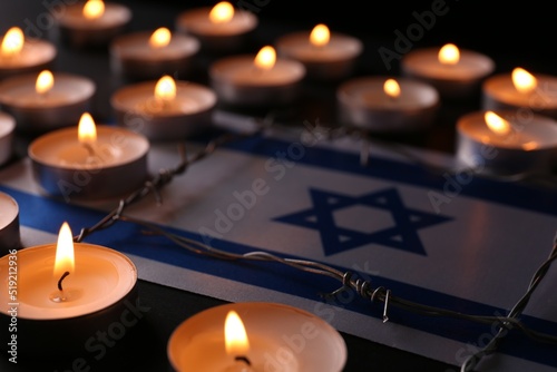 Flag of Israel, barbed wire and burning candles on black background. Holocaust memory day photo