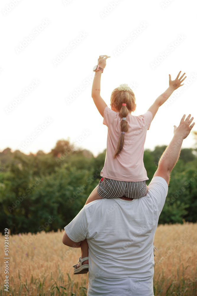 a girl on her father's back, against the background of a yellow field and green trees a girl on her father's back, against the background of a yellow field and green trees