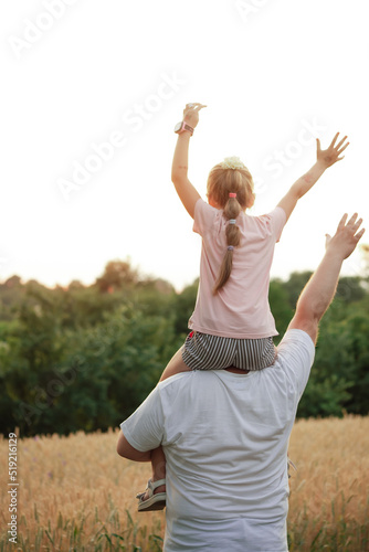 a girl on her father's back, against the background of a yellow field and green trees