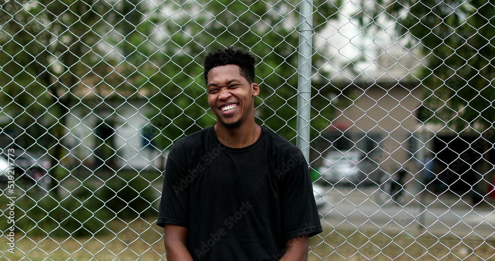 Smiling black guy leaning on metal fence standing casually outside