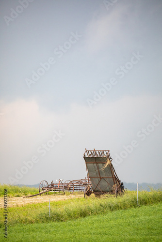 Hay farming equipment sitting out in an open green field under a cloudy sky | Amish country, Ohio