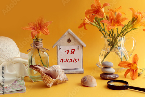 Calendar for August 18: decorative house with numbers 18, name of the month august in English, bouquets of daylilies, sea shells and stones, summer hat on an orange background, side view photo