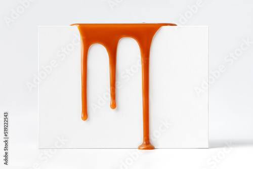 Dripping caramel drops of sweet caramel sauce on white podium on white background.  Melted caramel sauce drip, drops of sweet liquid toffee.