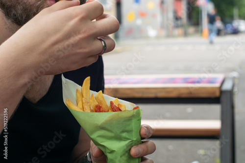 Obraz na płótnie Man eating some street food outside - french fries with ketchup in a paper cone. Caucasian bearded guy having fast food. w salonie