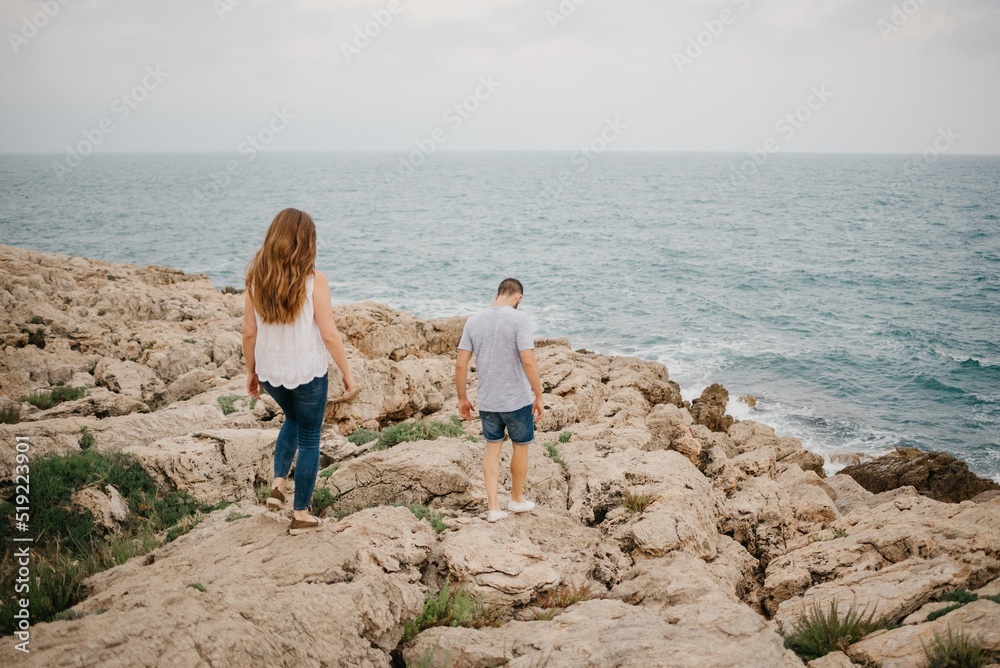 A man and his girlfriend are descending from the rocky hill to the sea in Spain