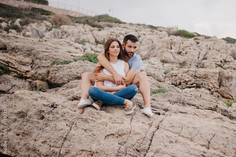 A man is holding his girlfriend while both are sitting on the rocks in Spain