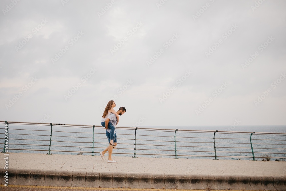 A man is carrying on his back a girl through the bridge near the sea in Spain.