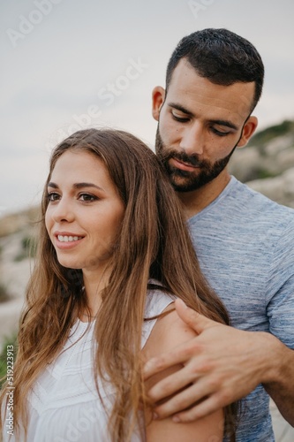 A Hispanic man is hugging a Latina girl on the rocky sea coast in Spain.
