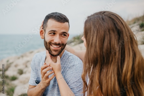 A girl is stroking with her hands the face of her boyfriend on the rocky hill