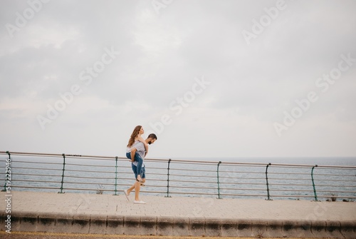 Obraz na płótnie A man is carrying on his back a girl through the bridge near the sea in Spain. w salonie