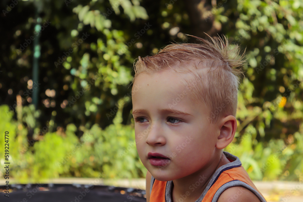 portrait of a cute boy of blonde European appearance close-up against the background of a green garden on a summer day selective focus portrait of a cute boy of blonde European appearance close-up against the background of a green garden on a summer day selective focus