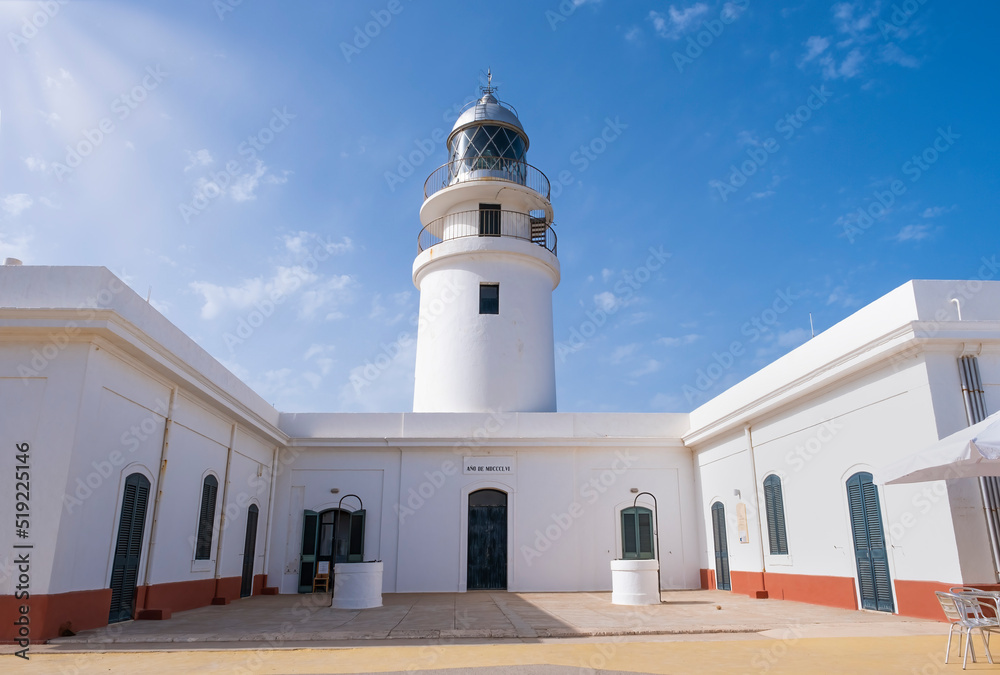 perspective view of a white lighthouse on a summer day with the blue sky illuminated by lateral sunbeams, Caballeria lighthouse in Menorca, Balearic Islands, Spain, horizontal